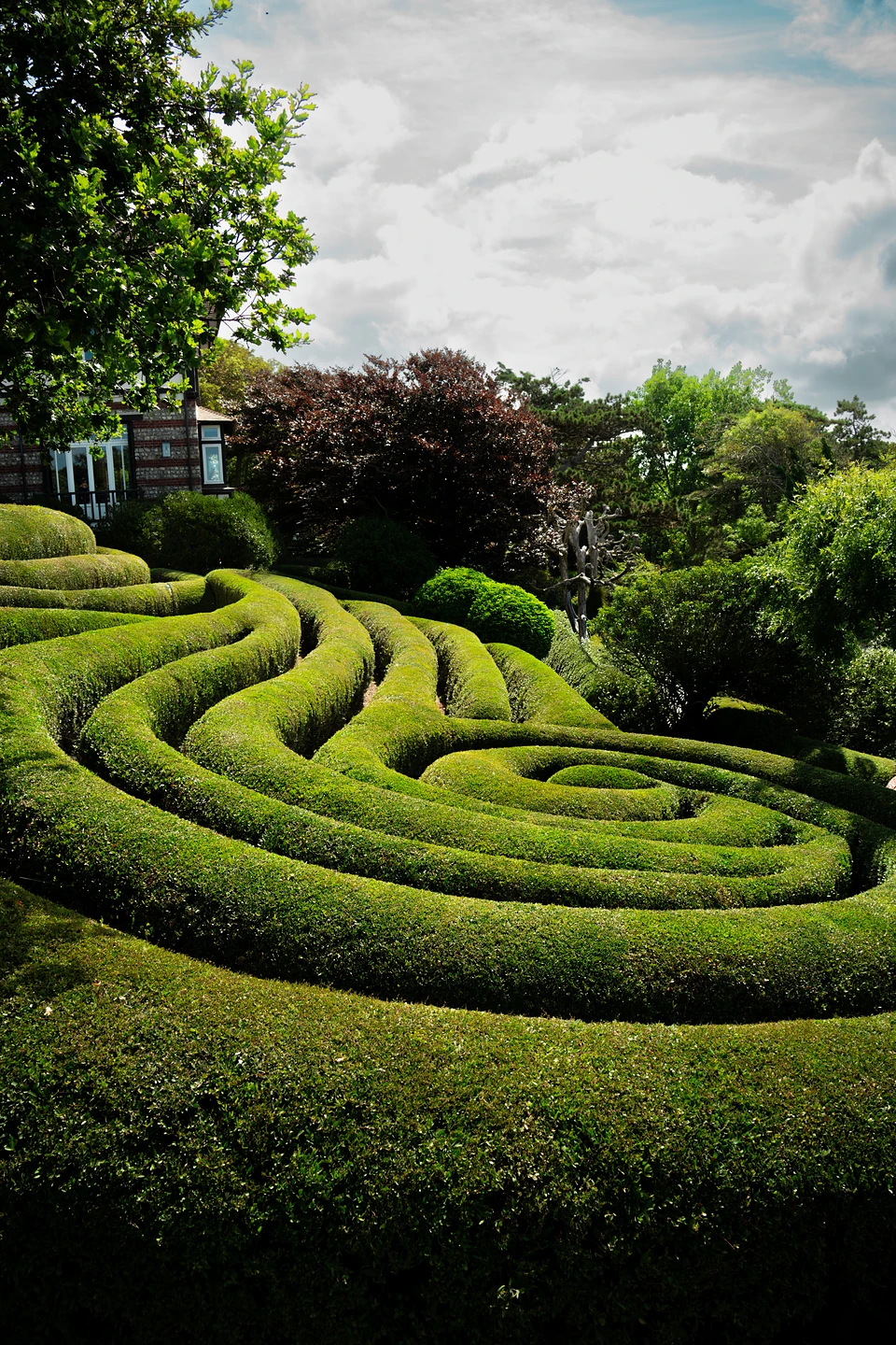 Clipped hedges coiling into a green spiral under a cloudy sky at Les Jardins d'Étretat