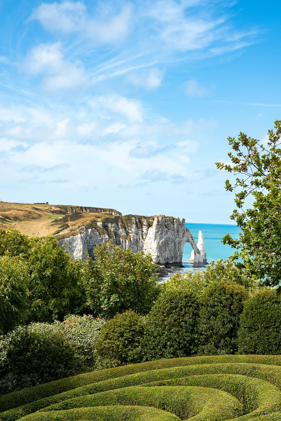 The chalk arch and the Needle seen over trees and wave-shaped hedges from Les Jardins d'Étretat