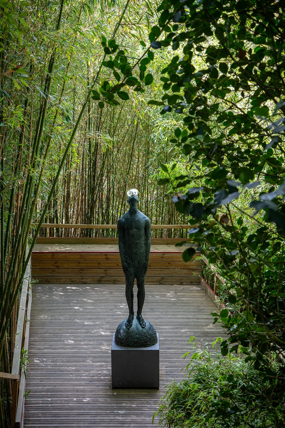 A slender dark statue on a plinth among bamboo at Les Jardins d'Étretat