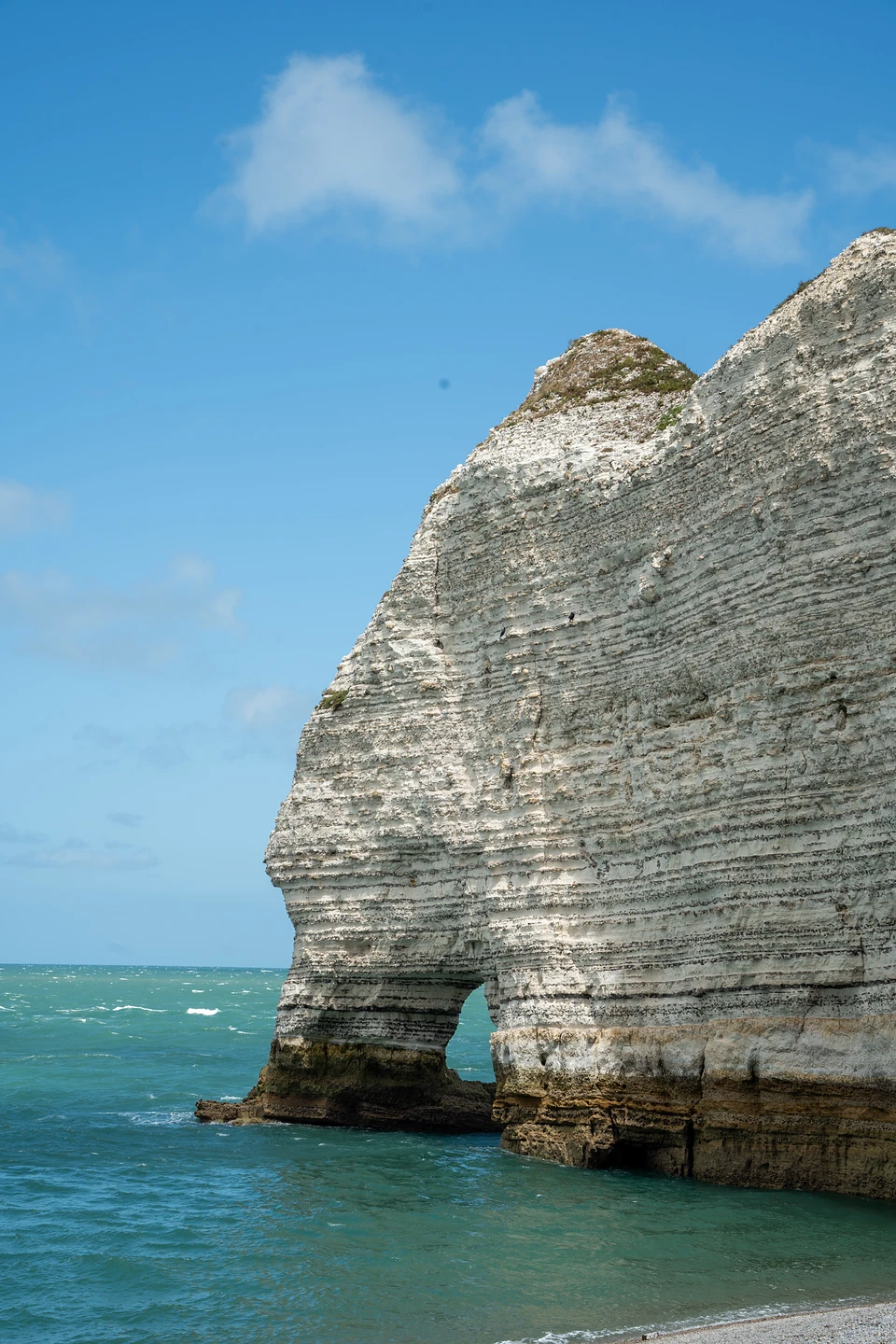A layered chalk cliff with a small arch at its foot, rising from turquoise sea