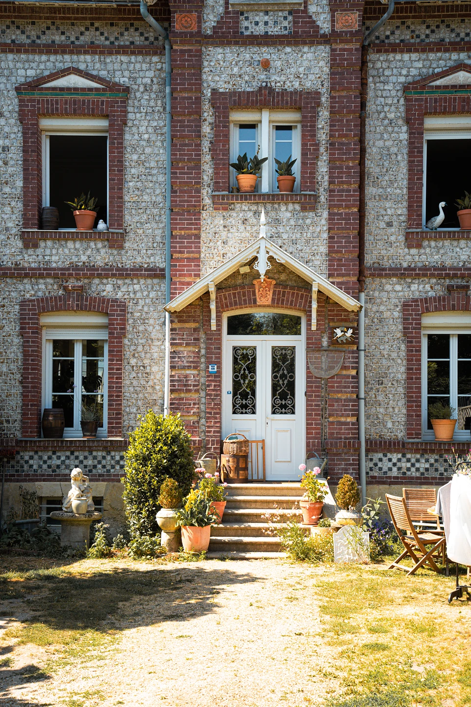 The porch and white double door of a brick-trimmed villa, steps lined with potted plants