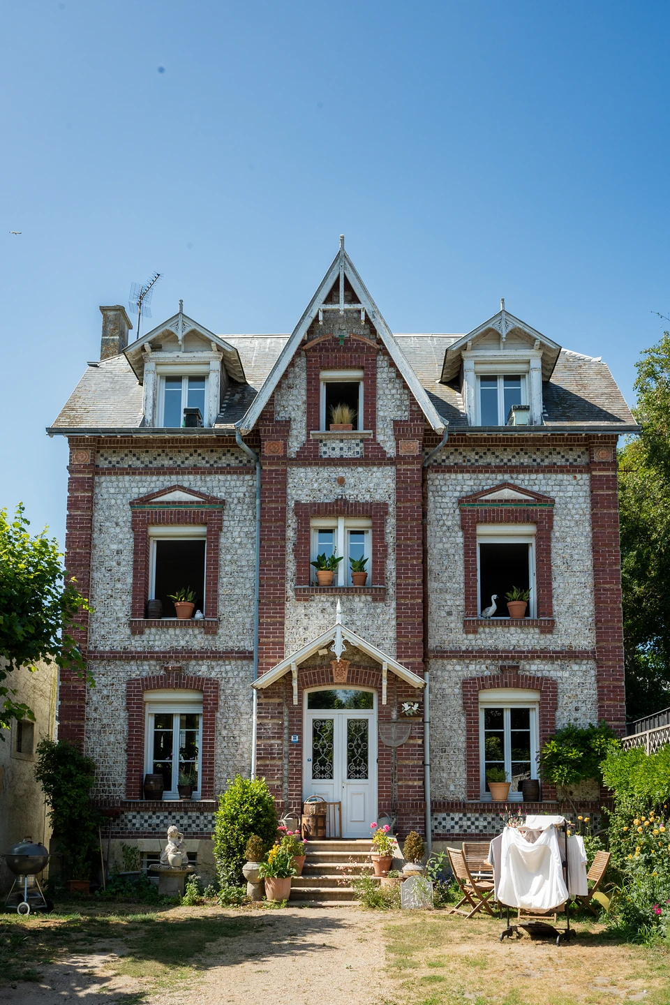 A brick and stone villa with a pointed central gable and dormers against a blue sky