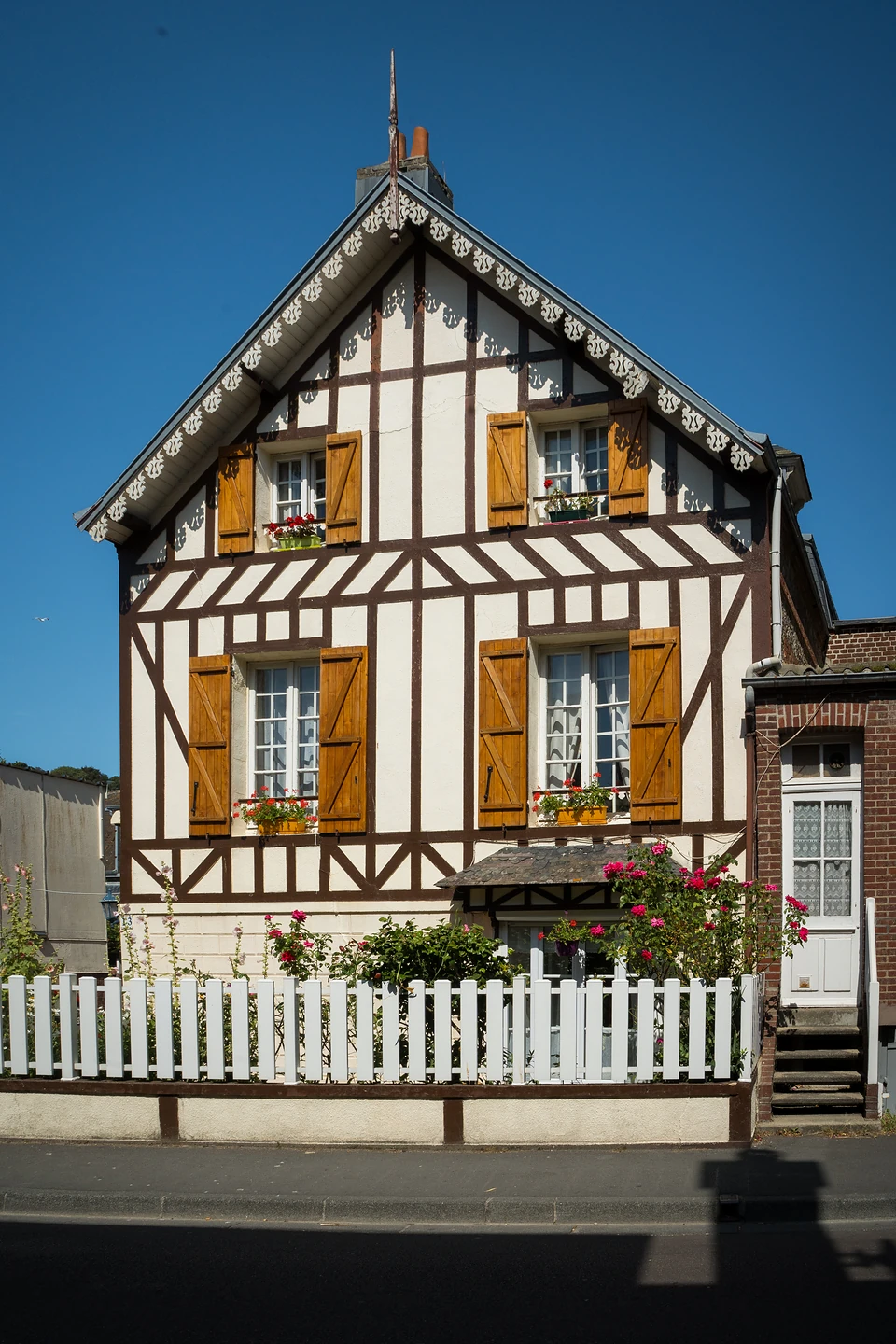A half-timbered house with wooden shutters and window boxes behind a white picket fence