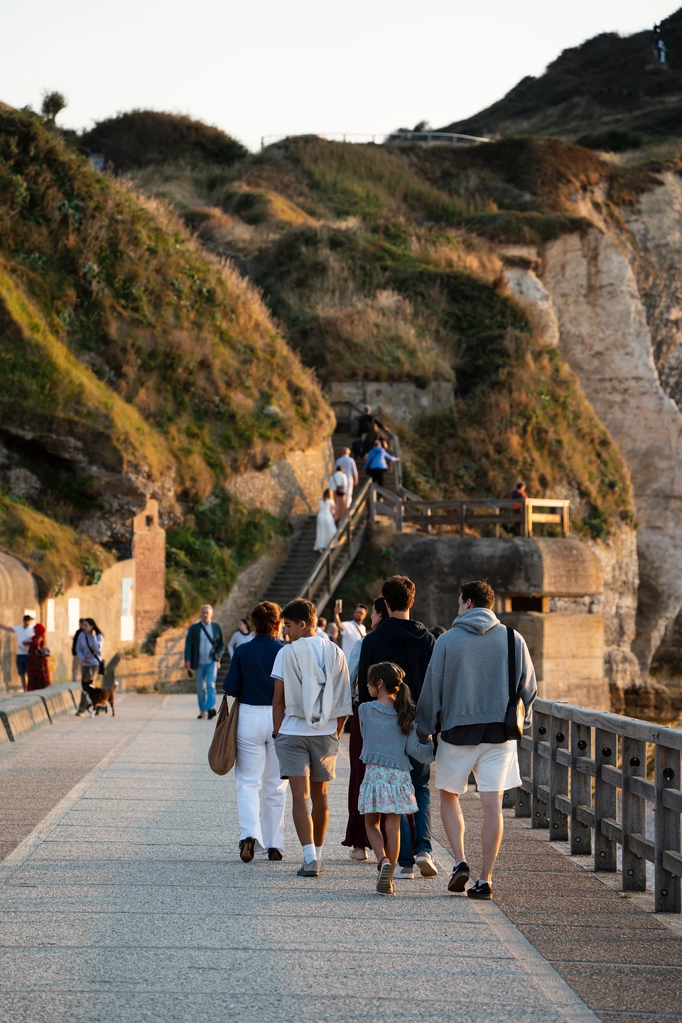 People walking the promenade toward the steps up the cliff, in warm evening light