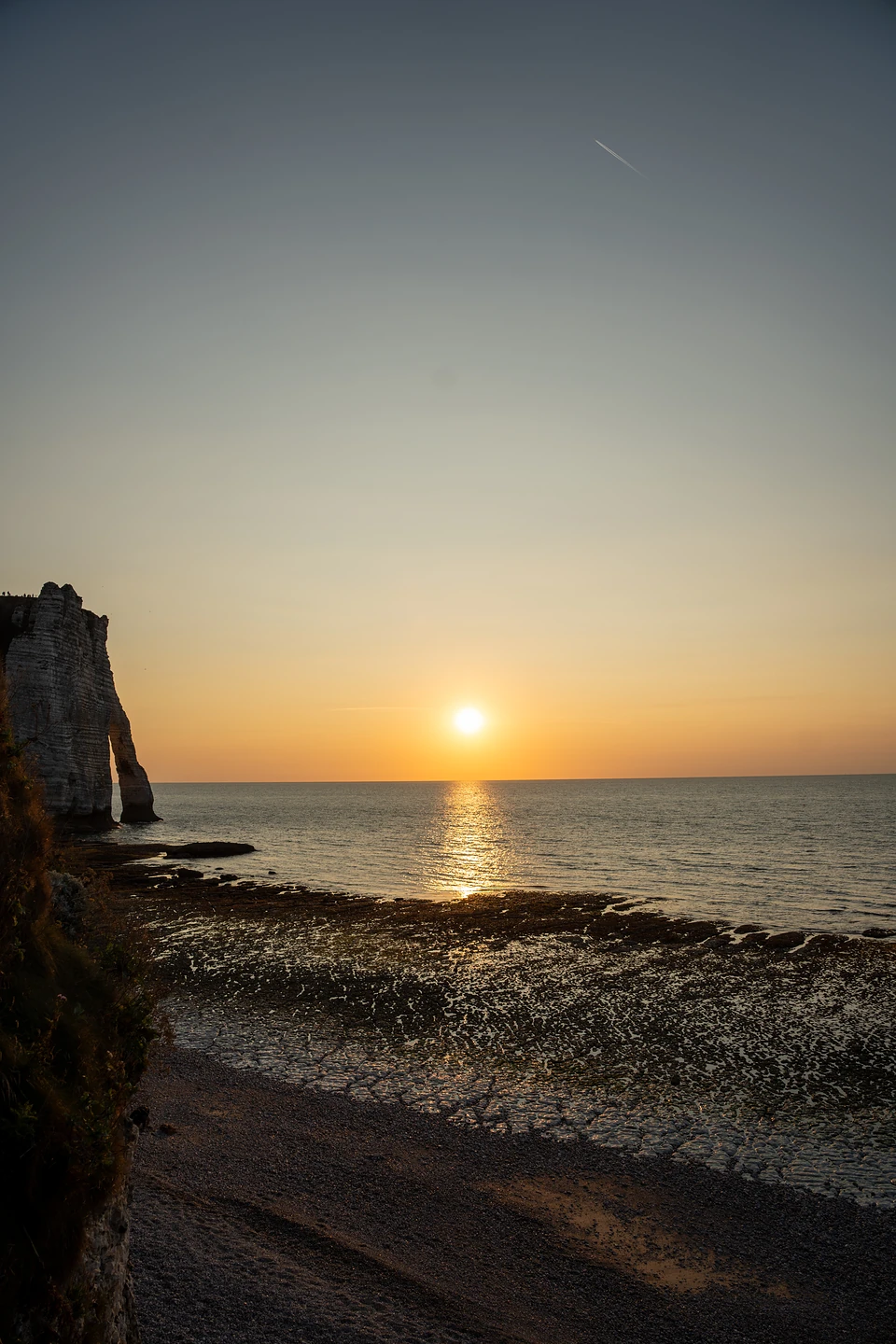 The sun sinking over the sea, the arch dark at left and wet rocks glinting below