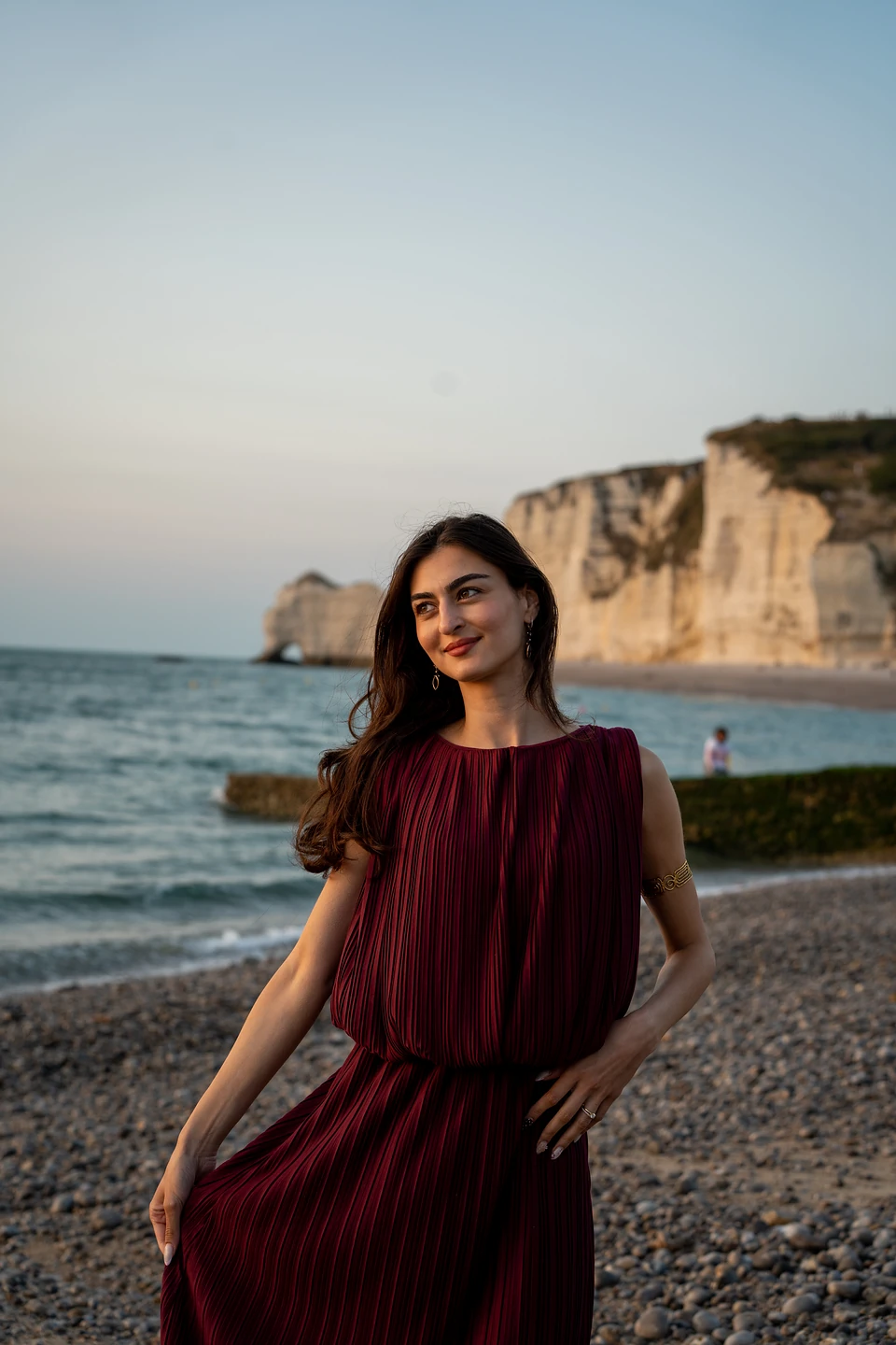One of us in a red pleated dress on the shingle, chalk cliffs in evening light