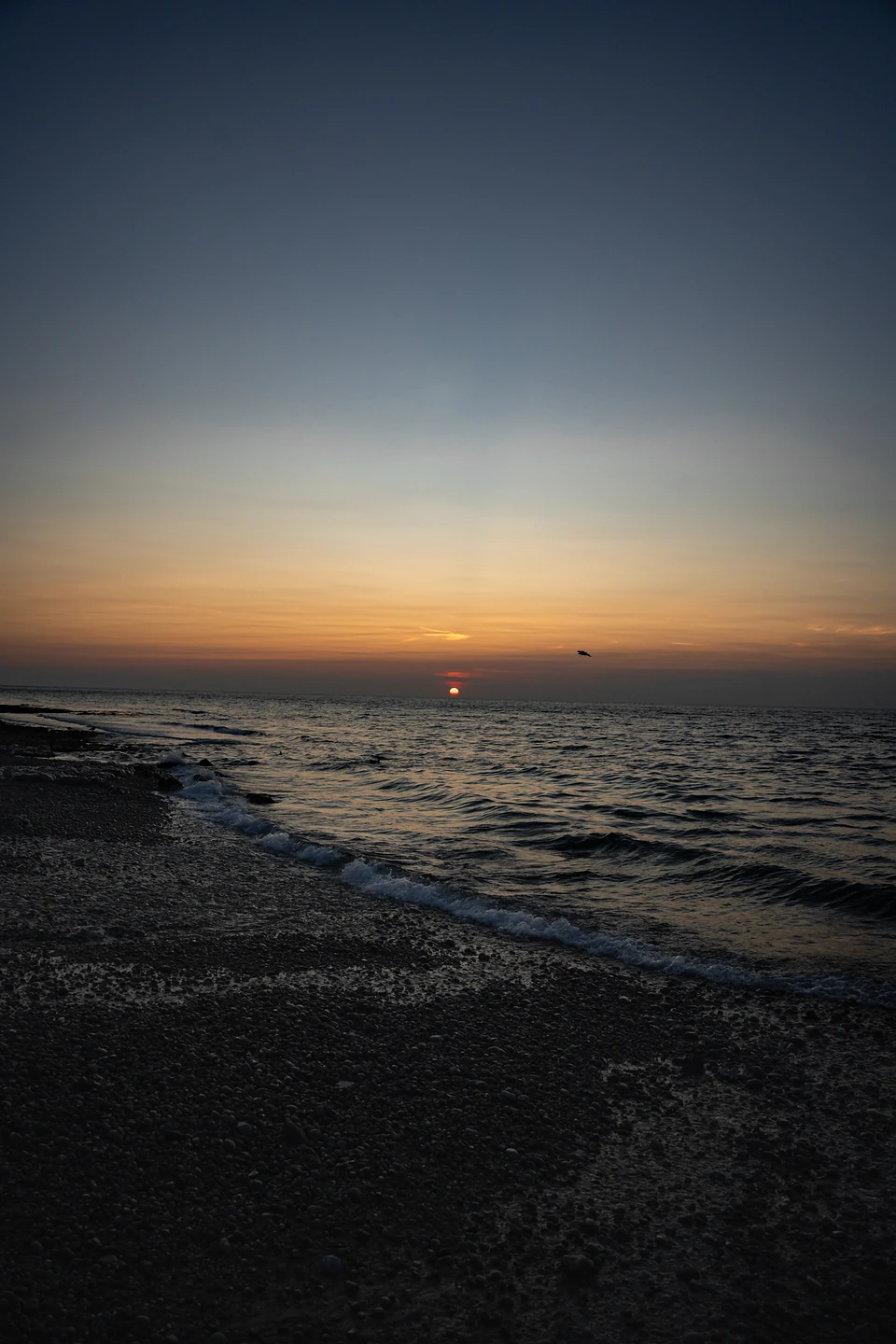 The last of the sun on the horizon, small waves washing up a dark shingle beach