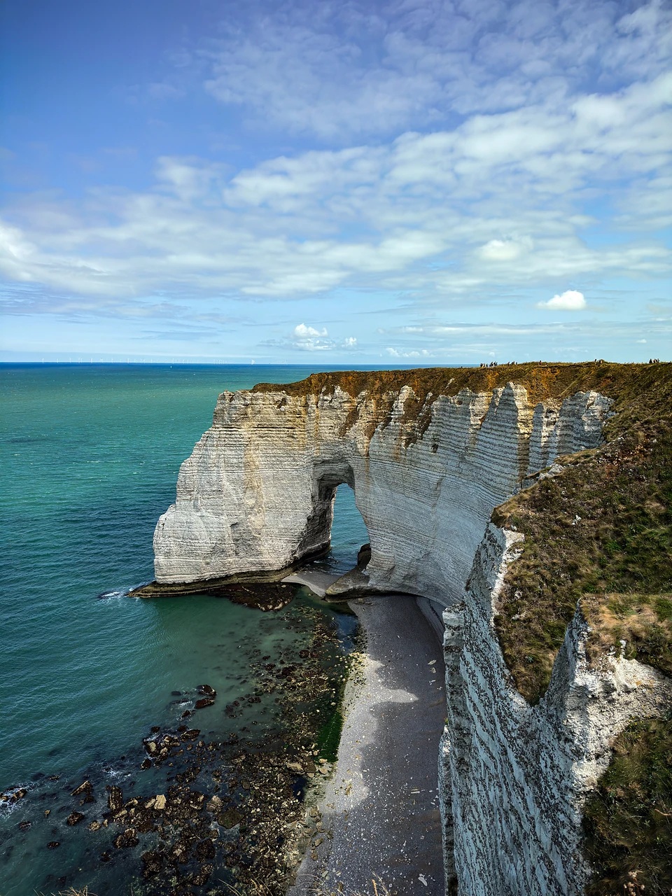A chalk arch under streaky cloud, a strip of beach and dark rocks at its foot