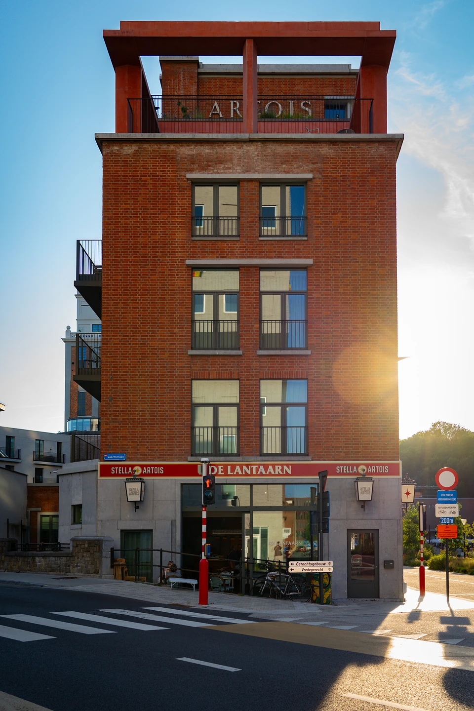 A tall brick building crowned with ‘Artois’ letters, the De Lantaarn café below in low sun