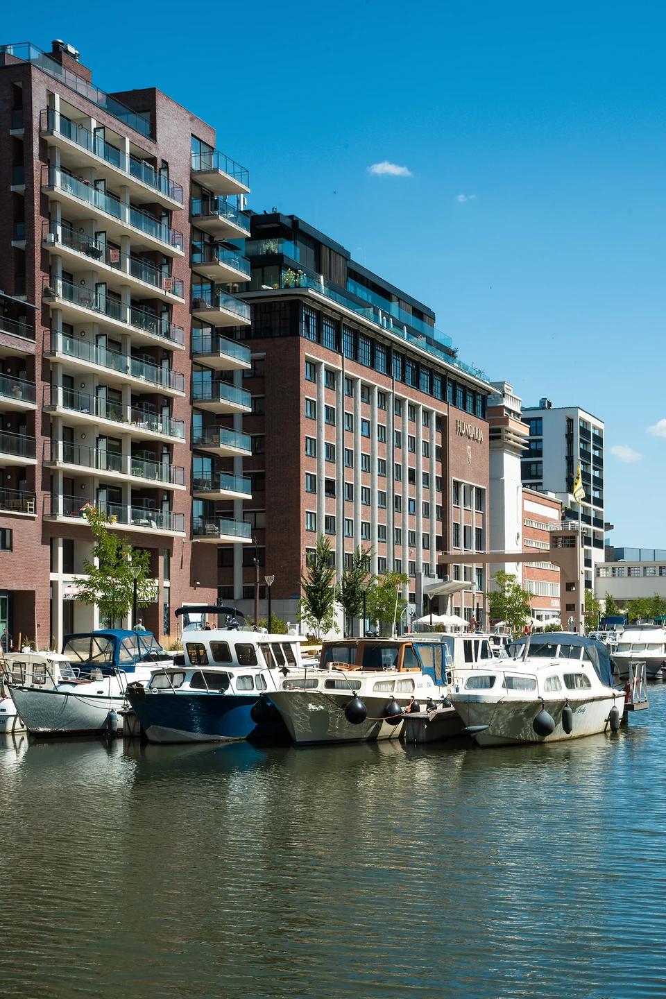 Motorboats moored along the Vaartkom quay below brick apartment blocks on a bright day