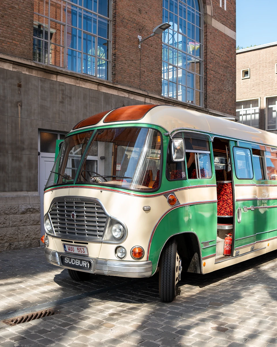 A vintage cream and green coach parked on cobbles beside a brick building with tall windows