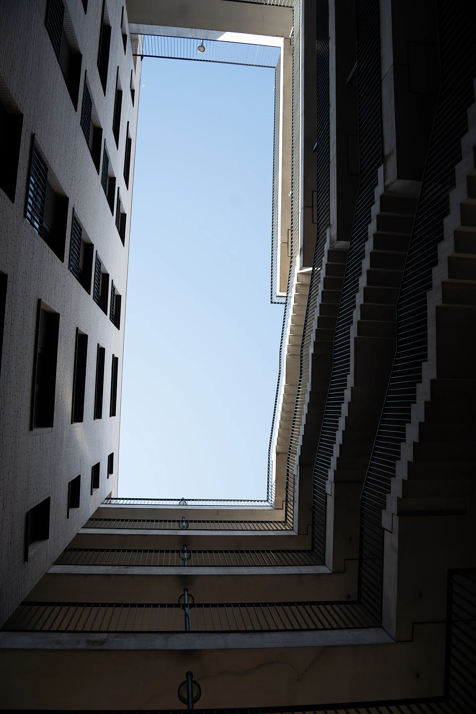 Looking up between pale walls and zigzag stairs to a rectangle of blue sky