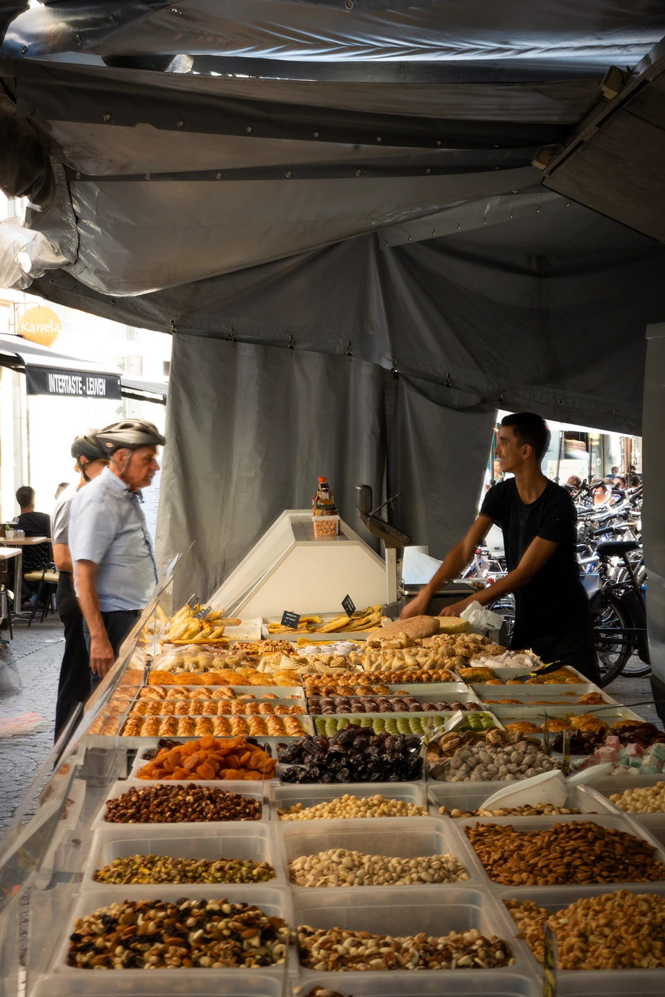A stall heaped with dried fruit, nuts and pastries, the vendor serving two customers
