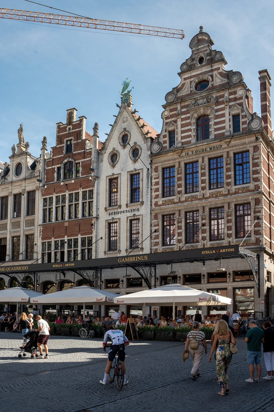Ornate gabled facades above the busy Gambrinus terraces, a cyclist in racing kit crossing the cobbles