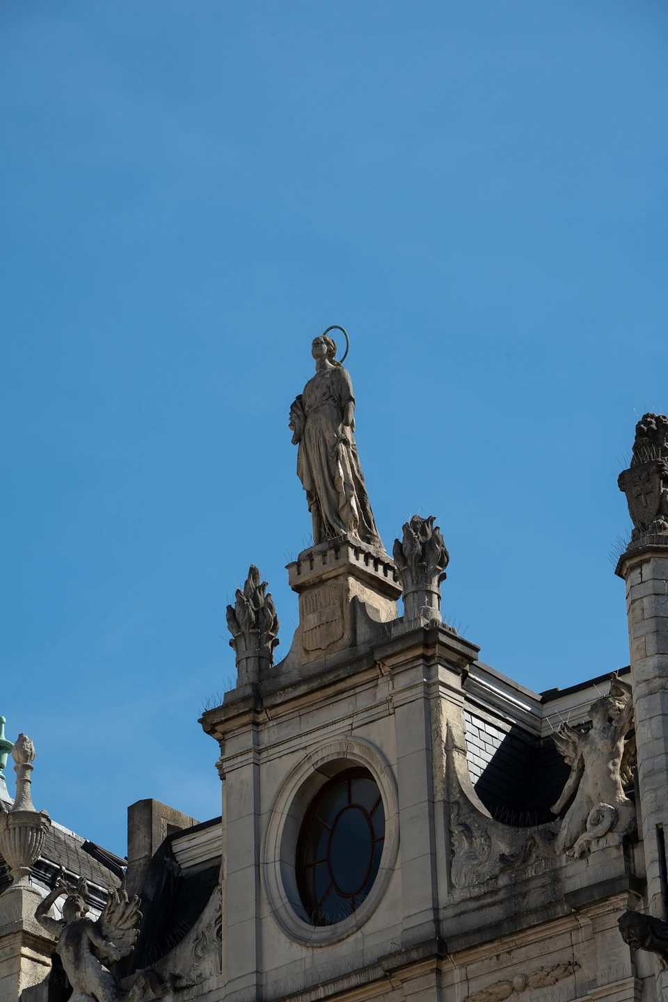 A haloed stone figure atop a carved gable with a round window, against deep blue sky