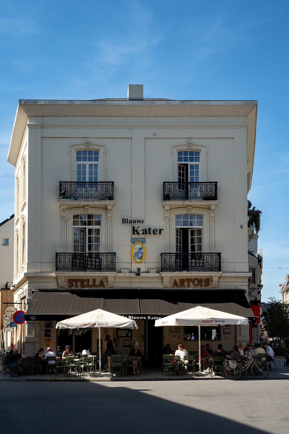 The white facade of the Blauwe Kater, its terrace of green chairs under white parasols