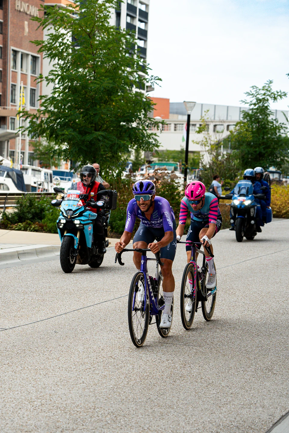 Two riders pass the Vaartkom on the Renewi Tour’s last day, race motorbikes close behind