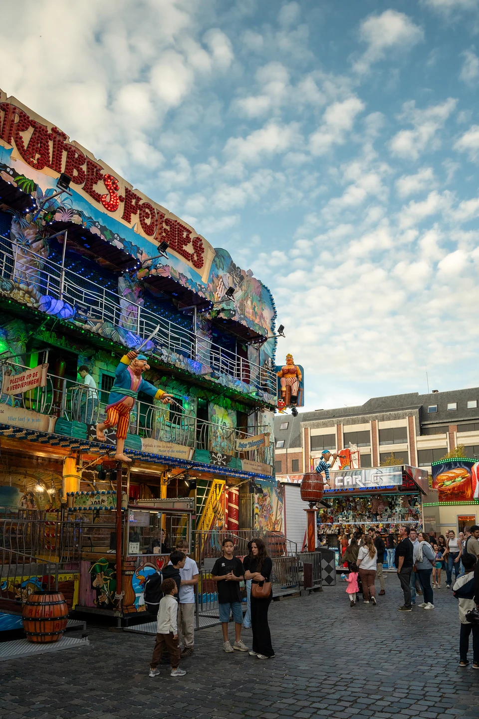 A pirate-themed funhouse with painted figures on its balconies, visitors strolling the cobbles below