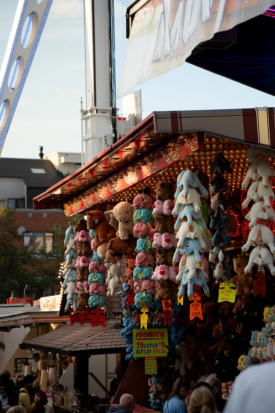 Columns of plush toys hanging from a lottery stall’s bulb-lit eaves, a ‘Promotie’ sign below