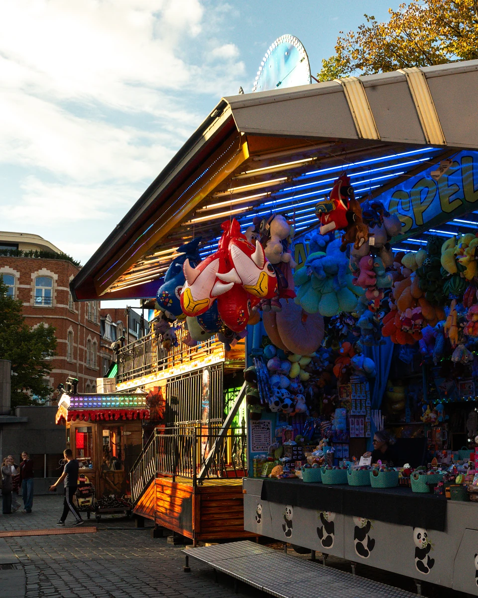 Balloons and plush prizes crowding a stall painted with pandas, lit by low evening sun