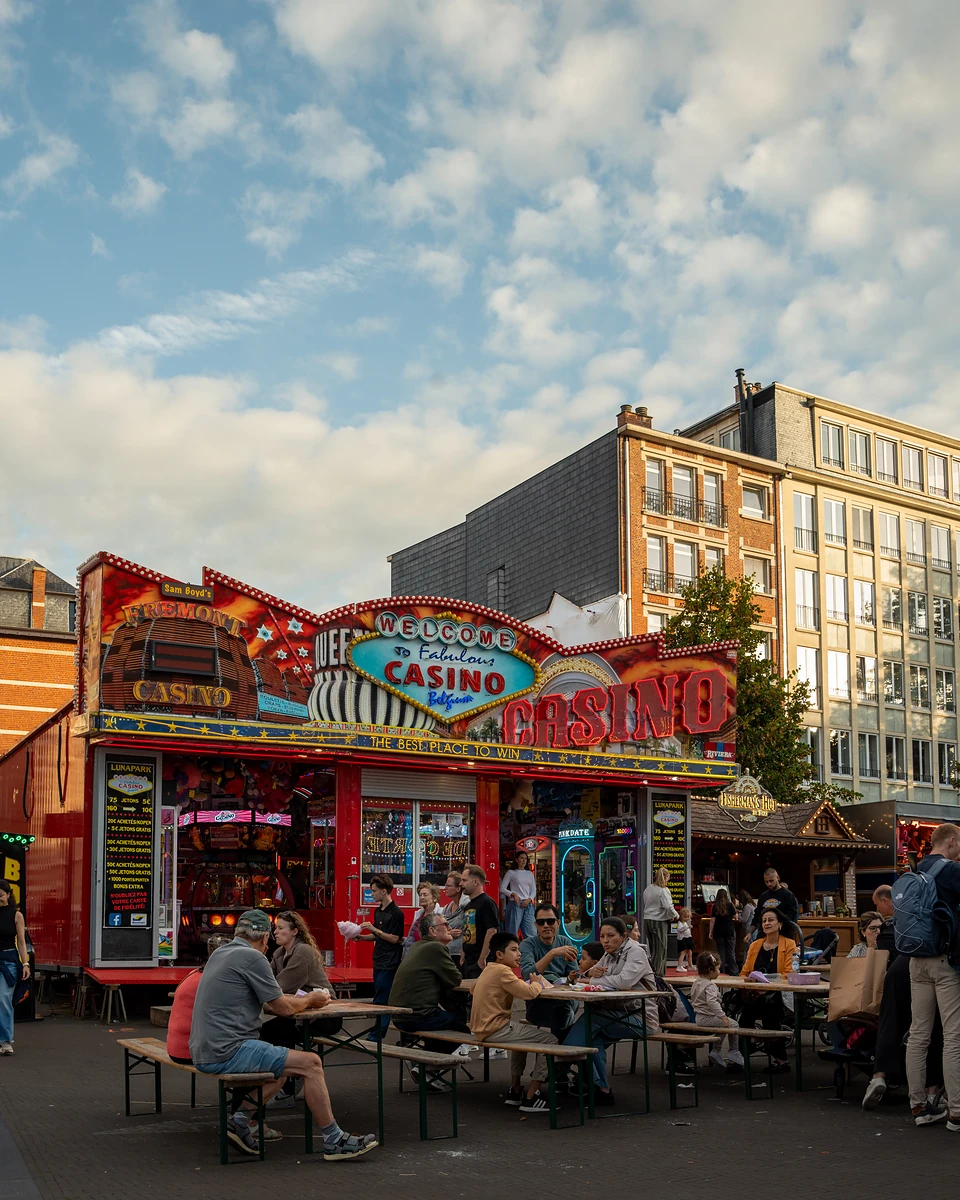 People at picnic tables in front of a ‘Casino’ arcade, apartment blocks catching the evening light