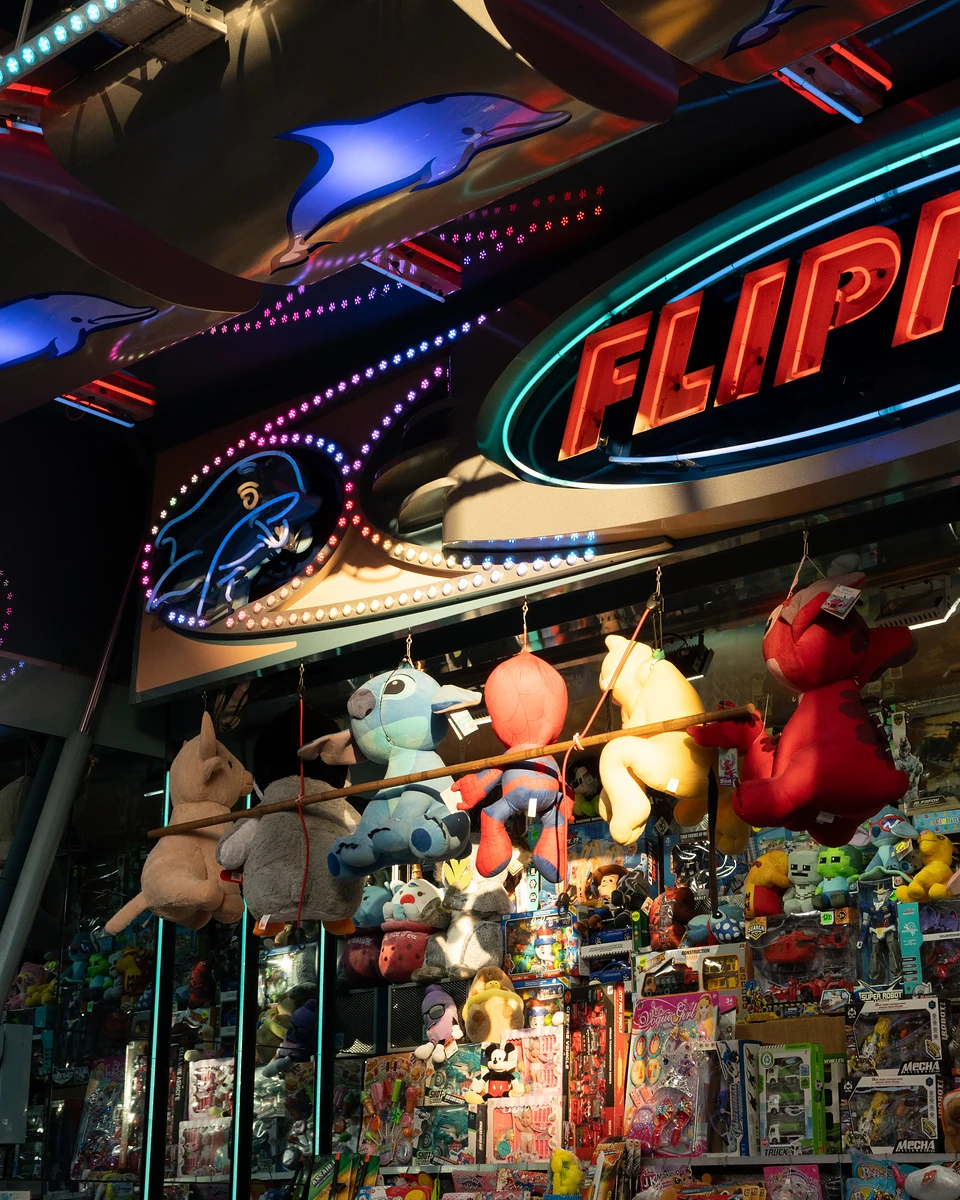 Plush prizes strung on a pole beneath the ‘Flipper’ neon and blue dolphin lights