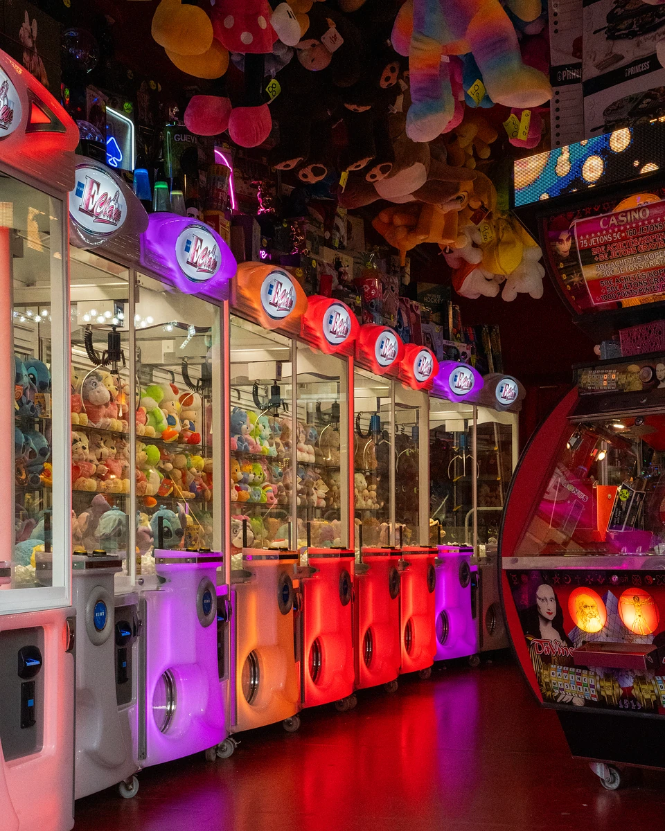 A row of claw machines glowing pink, orange, red and purple in a dim arcade