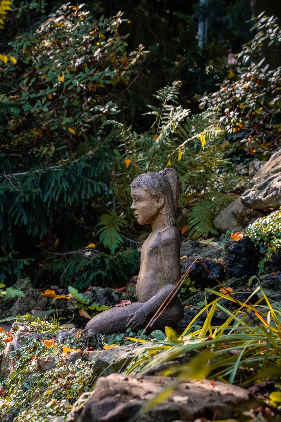 A carved kneeling figure with a ponytail among ferns and rocks