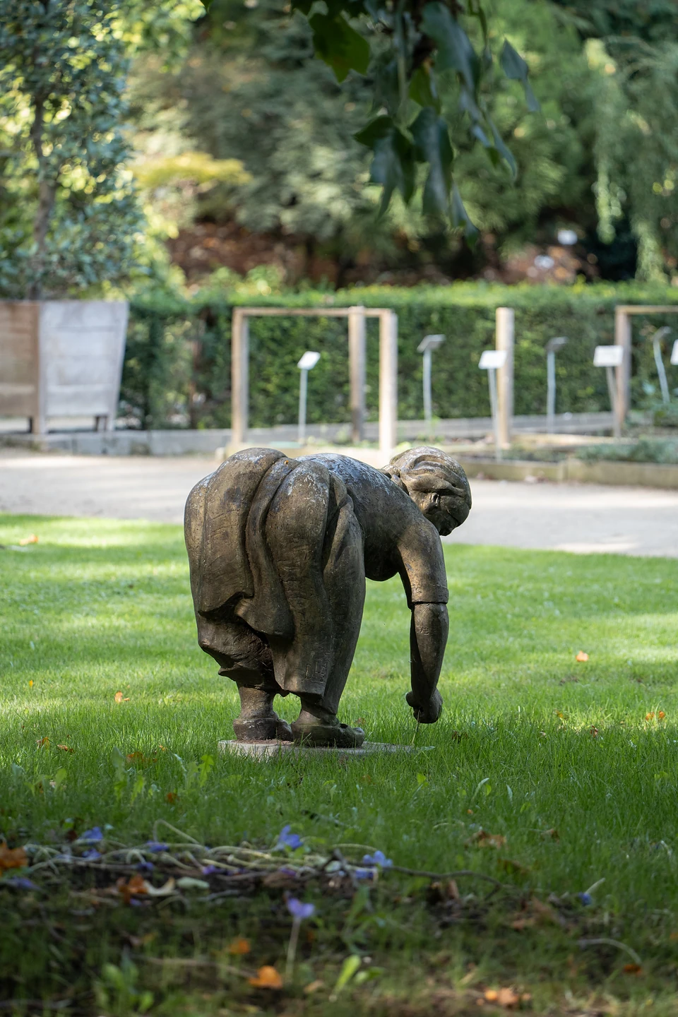 A dark sculpture of a figure in a long skirt stooping towards the lawn