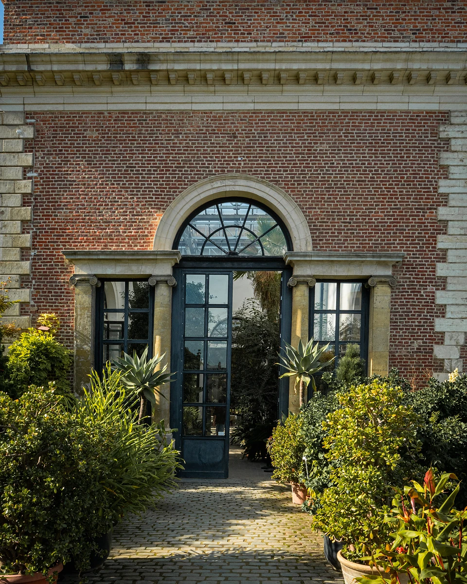 An arched fanlight over a tall glass door between stone columns, potted plants on the cobbles