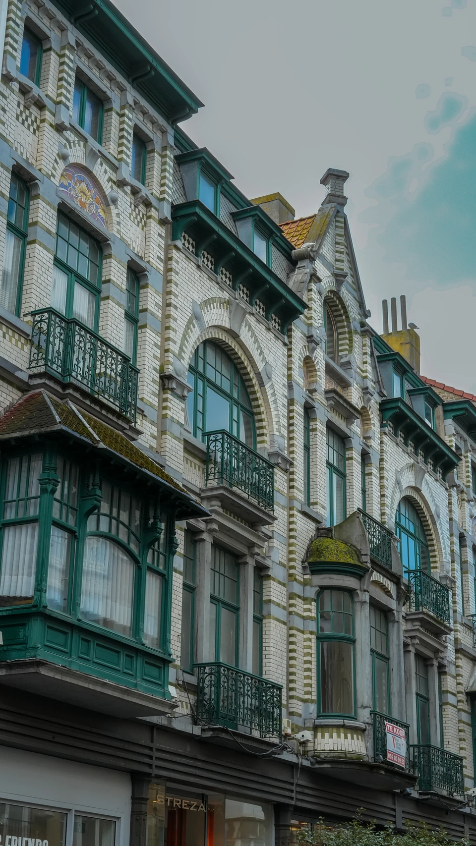 Townhouse facades of banded cream and yellow brick with green bay windows and wrought-iron balconies