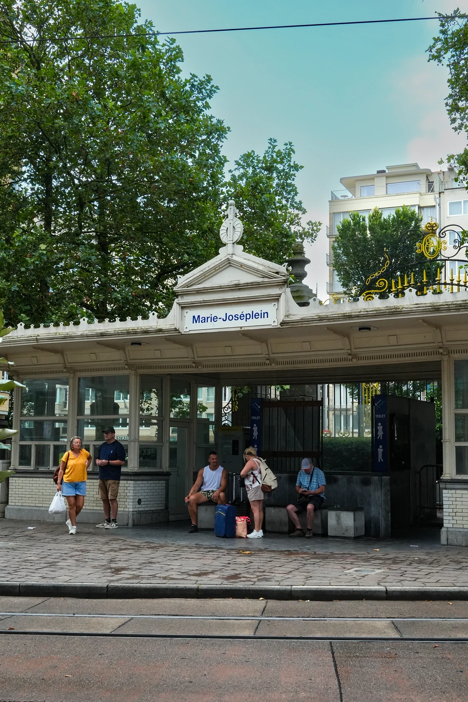 People waiting with luggage under the white 'Marie-Joséplein' shelter beside the tram tracks