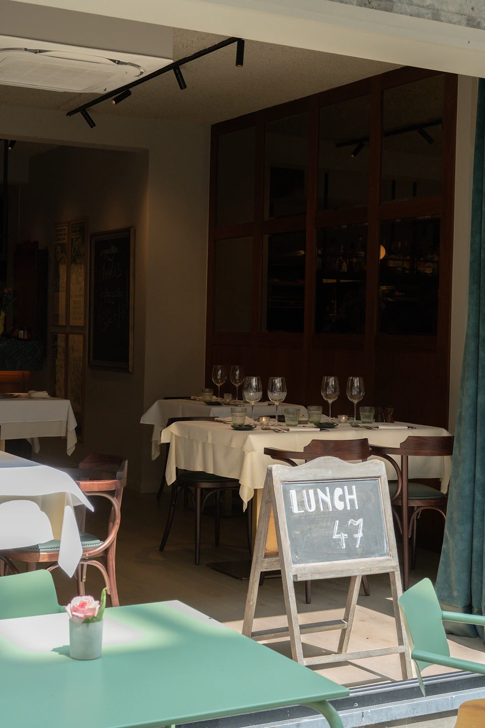 A chalkboard reading 'Lunch 47' at an open restaurant front, tables laid in white beyond