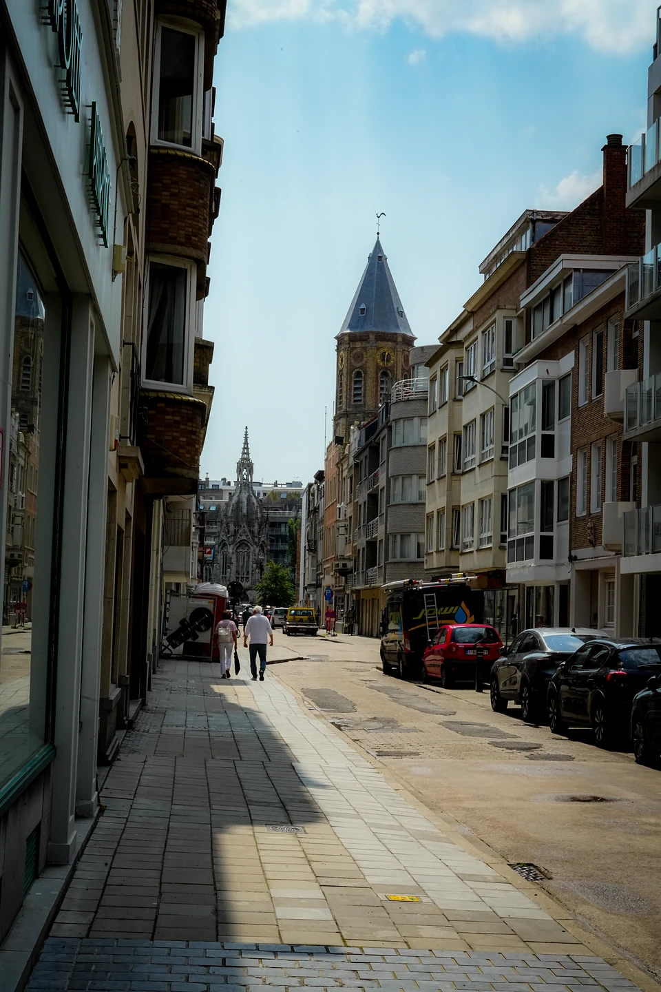 A quiet street leading to a pointed slate-roofed tower, a Gothic-style church spire beyond