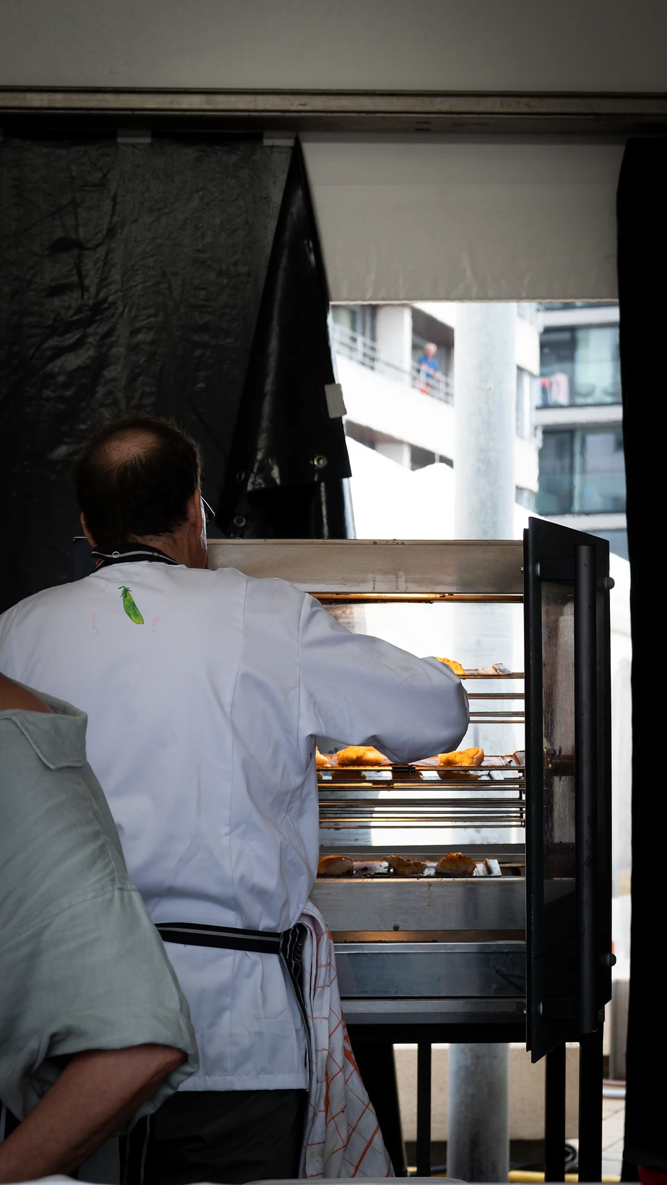 A cook seen from behind tending trays of golden food in a glass-fronted oven