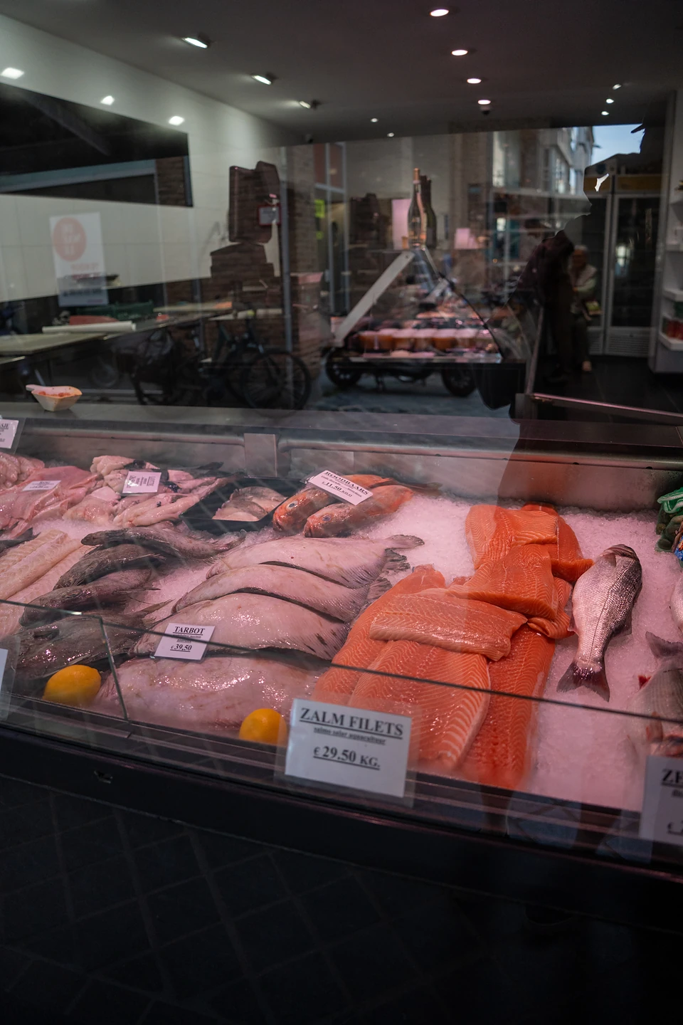 Salmon fillets, whole fish and lemons on ice in a fishmonger's counter, with price cards