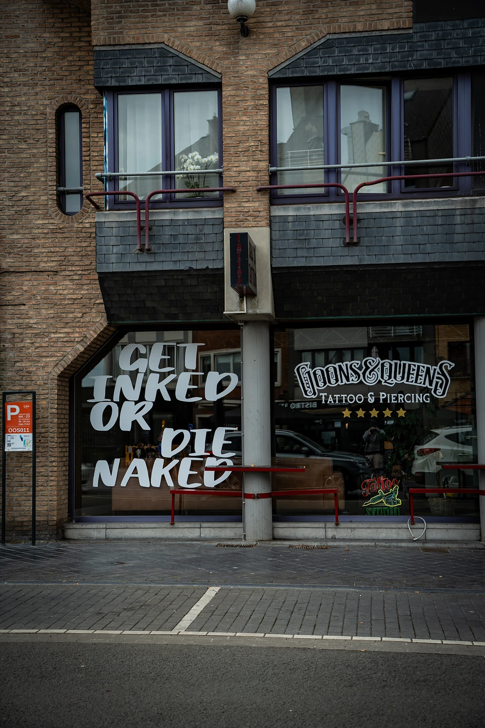 'Get inked or die naked' painted across a tattoo shop window in a brick building