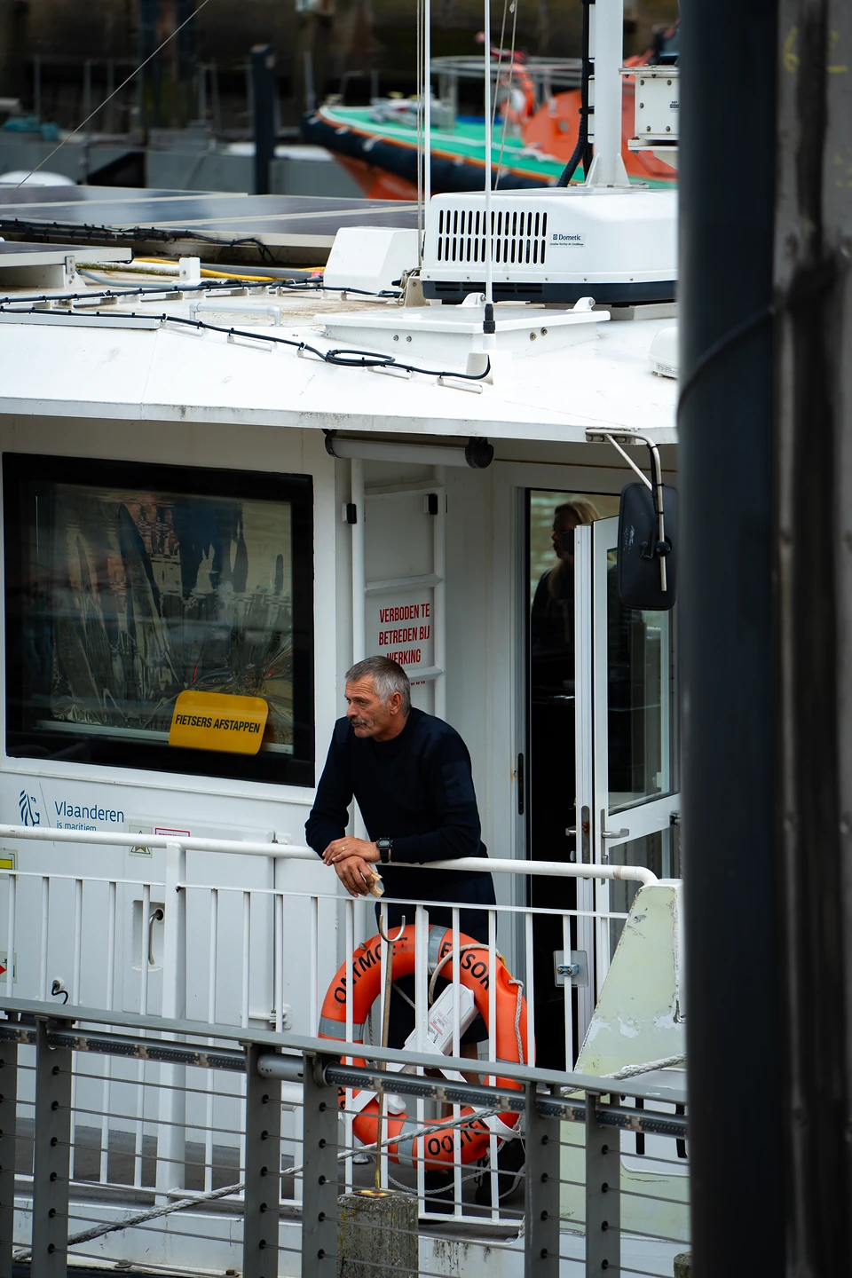 A man leaning on the rail of the white harbour ferry beside an orange lifebuoy
