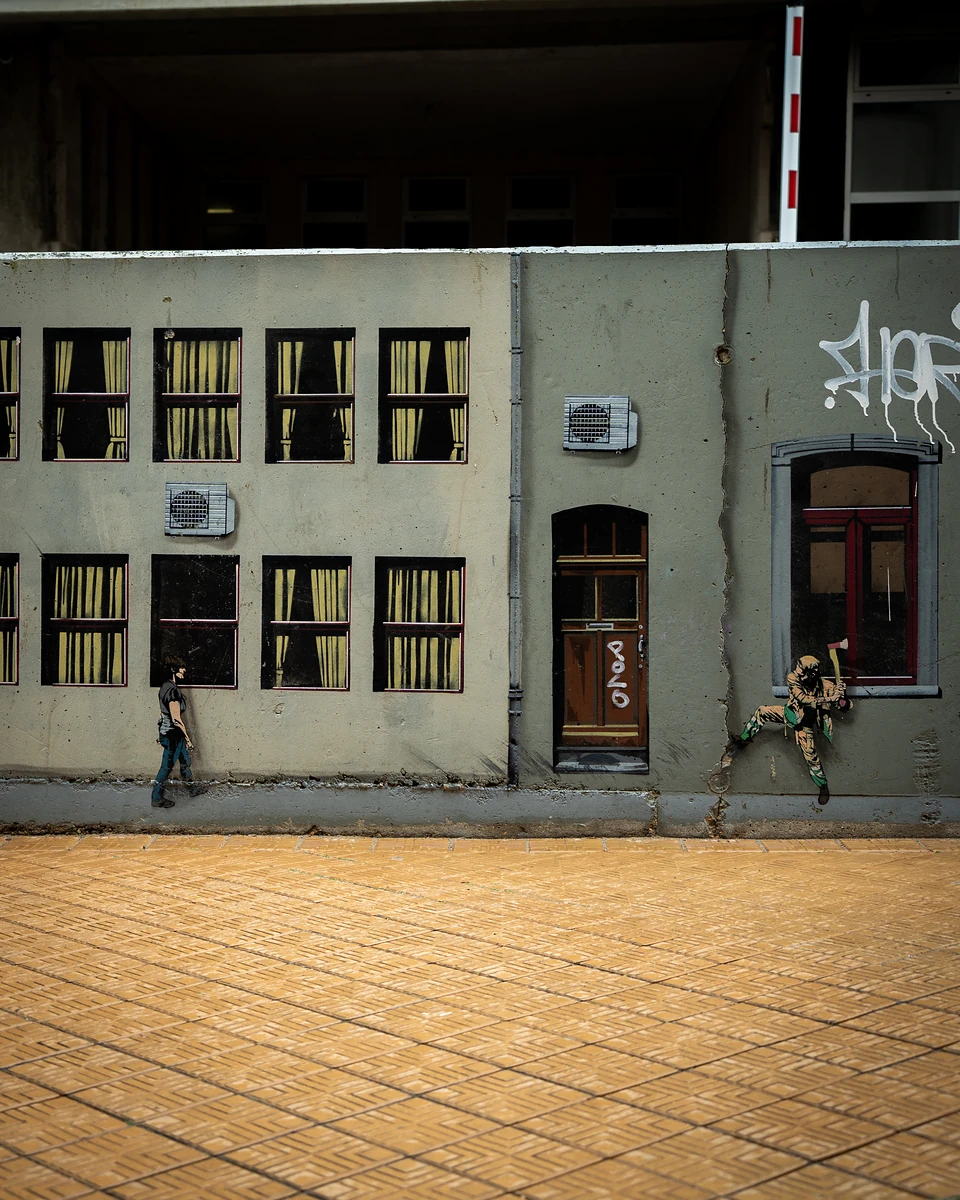 A grey wall painted with curtained windows and a door, with tiny figures walking and climbing