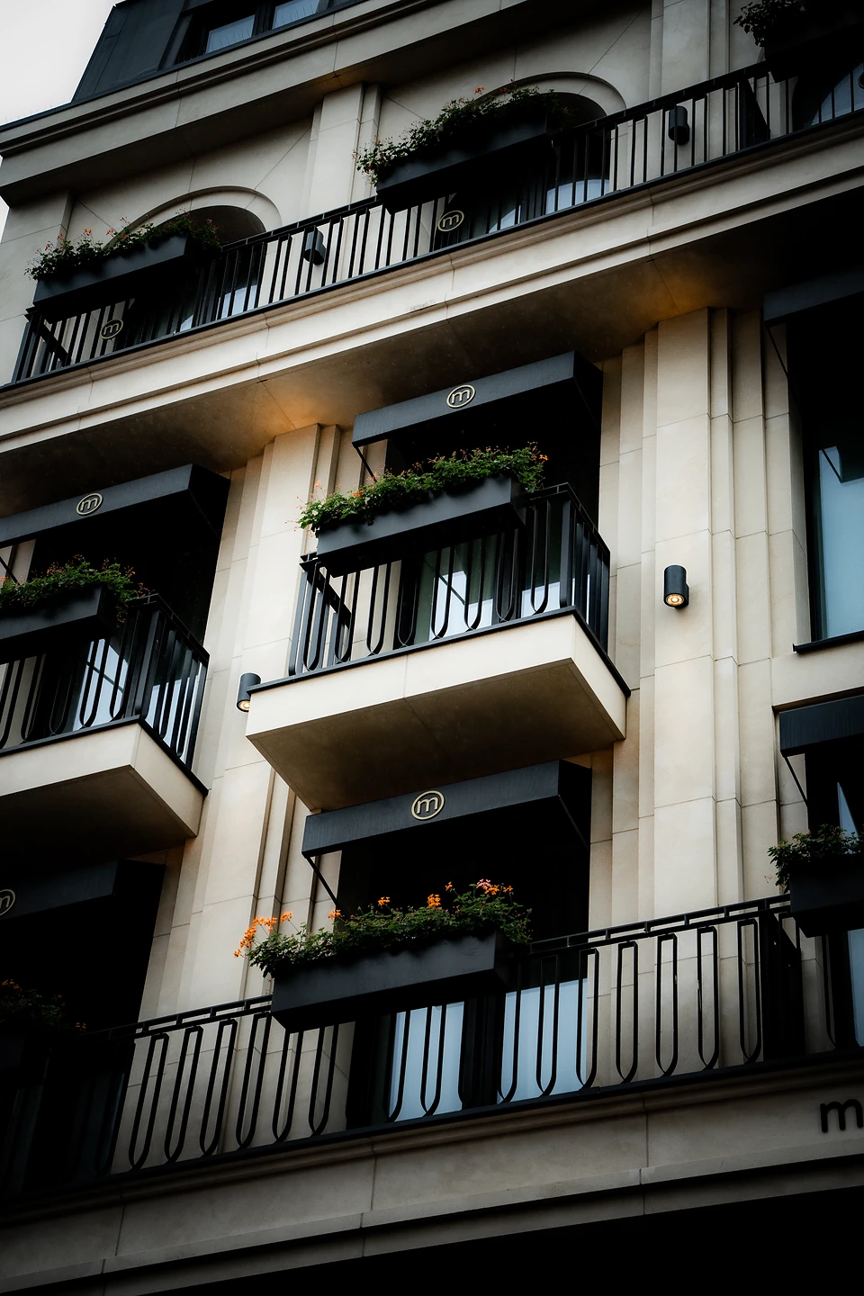 Black awnings marked with an 'm' over balconies and flower boxes on a cream stone facade