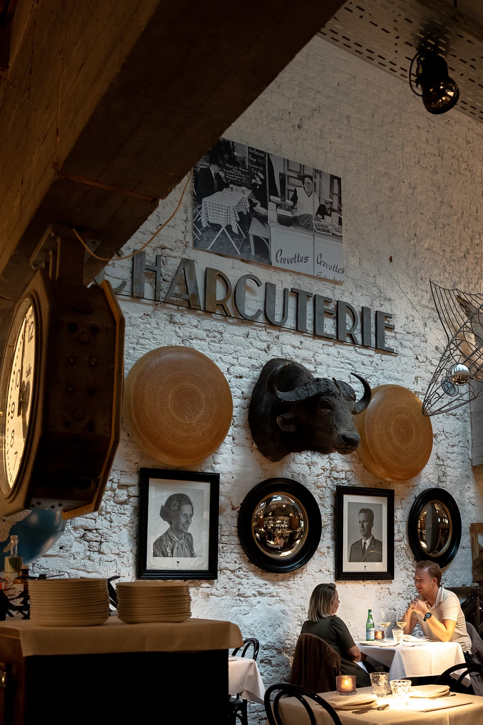 'Charcuterie' in dark letters on whitewashed brick, a buffalo head, mirrors and portraits above two diners