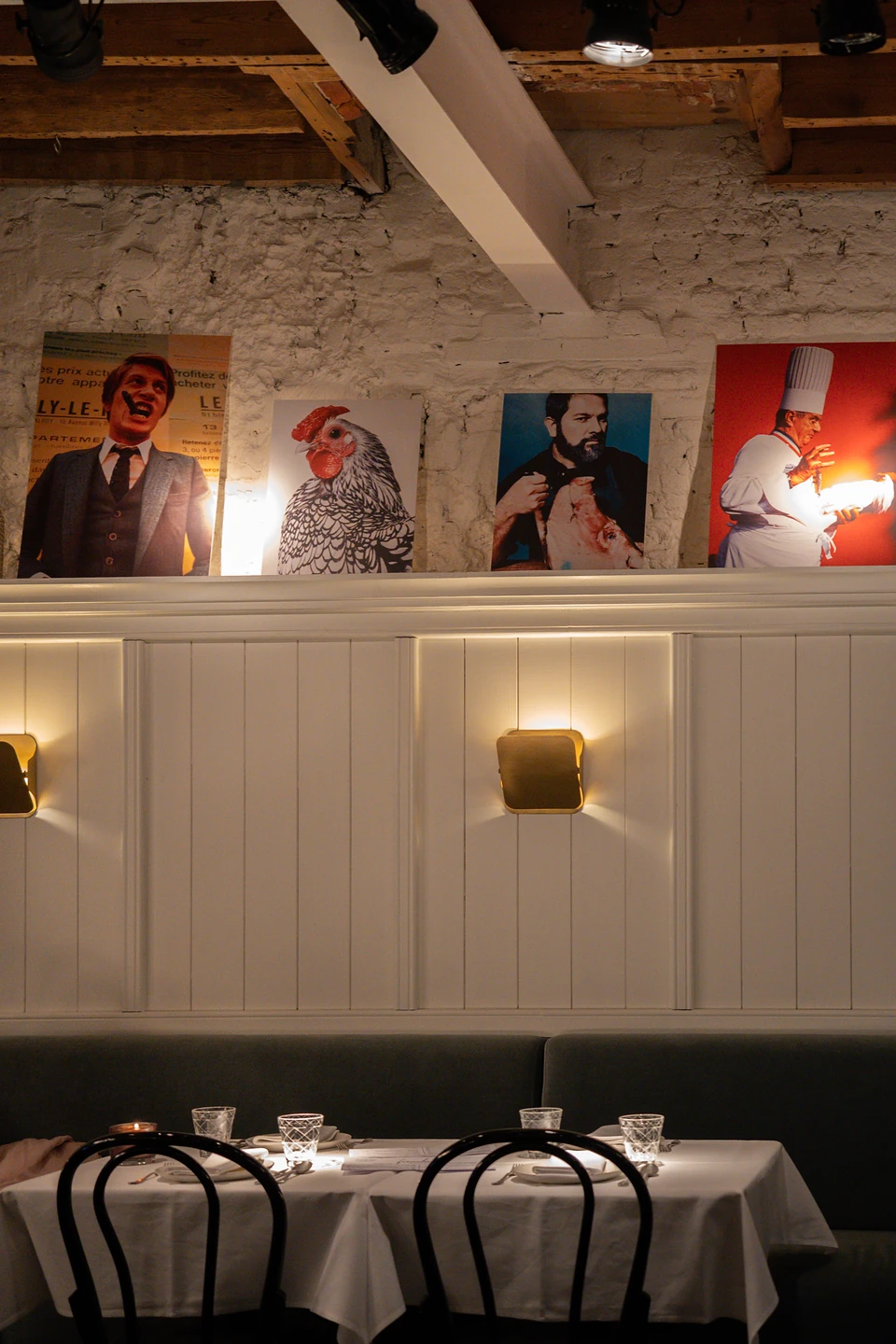 Four posters, a rooster and a chef among them, above white panelling and laid tables
