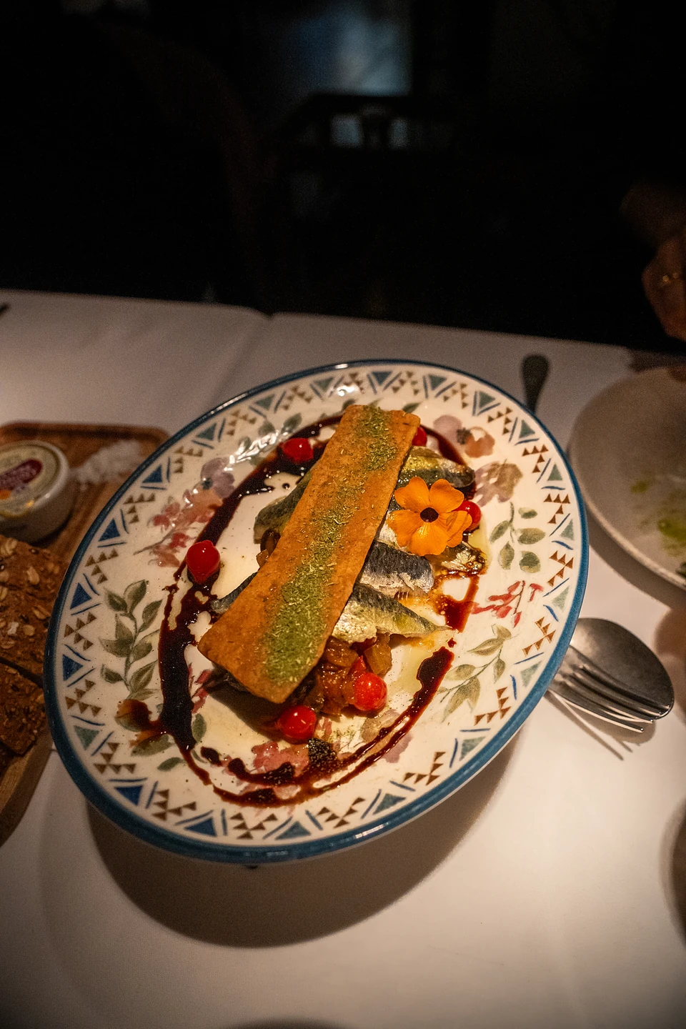 Silvery fish fillets under a long crisp wafer and an orange flower on a patterned plate