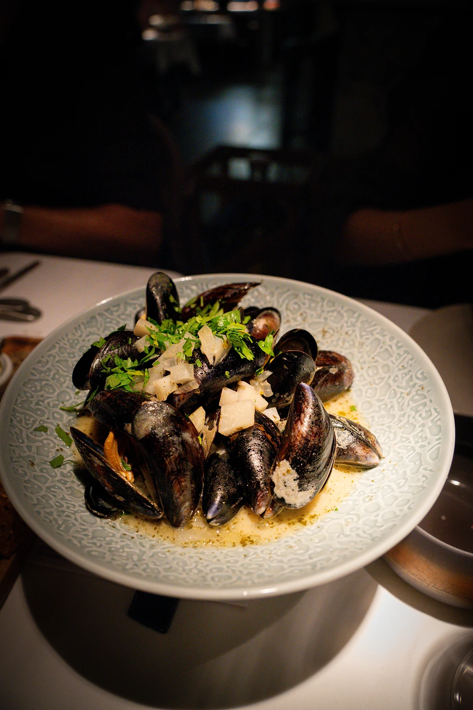 A bowl of moules with chopped parsley and diced vegetables in a golden broth