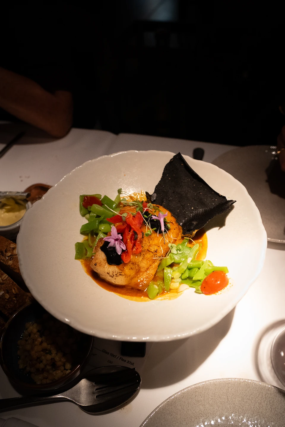 Seared fish with red pepper, edible flowers and a black crisp in an orange sauce