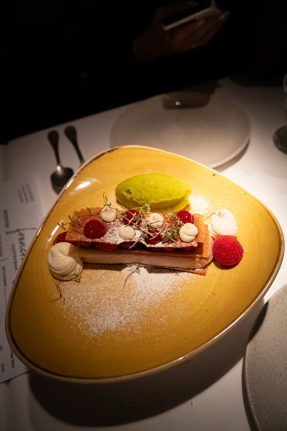 Layered pastry with raspberries and cream beside a green sorbet on a yellow plate