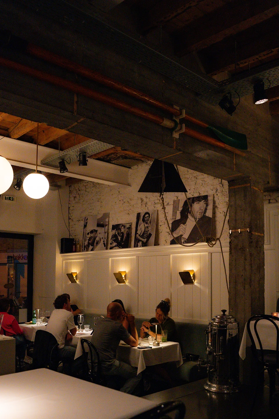 Diners at tables along the banquette beneath black-and-white photographs and globe lamps