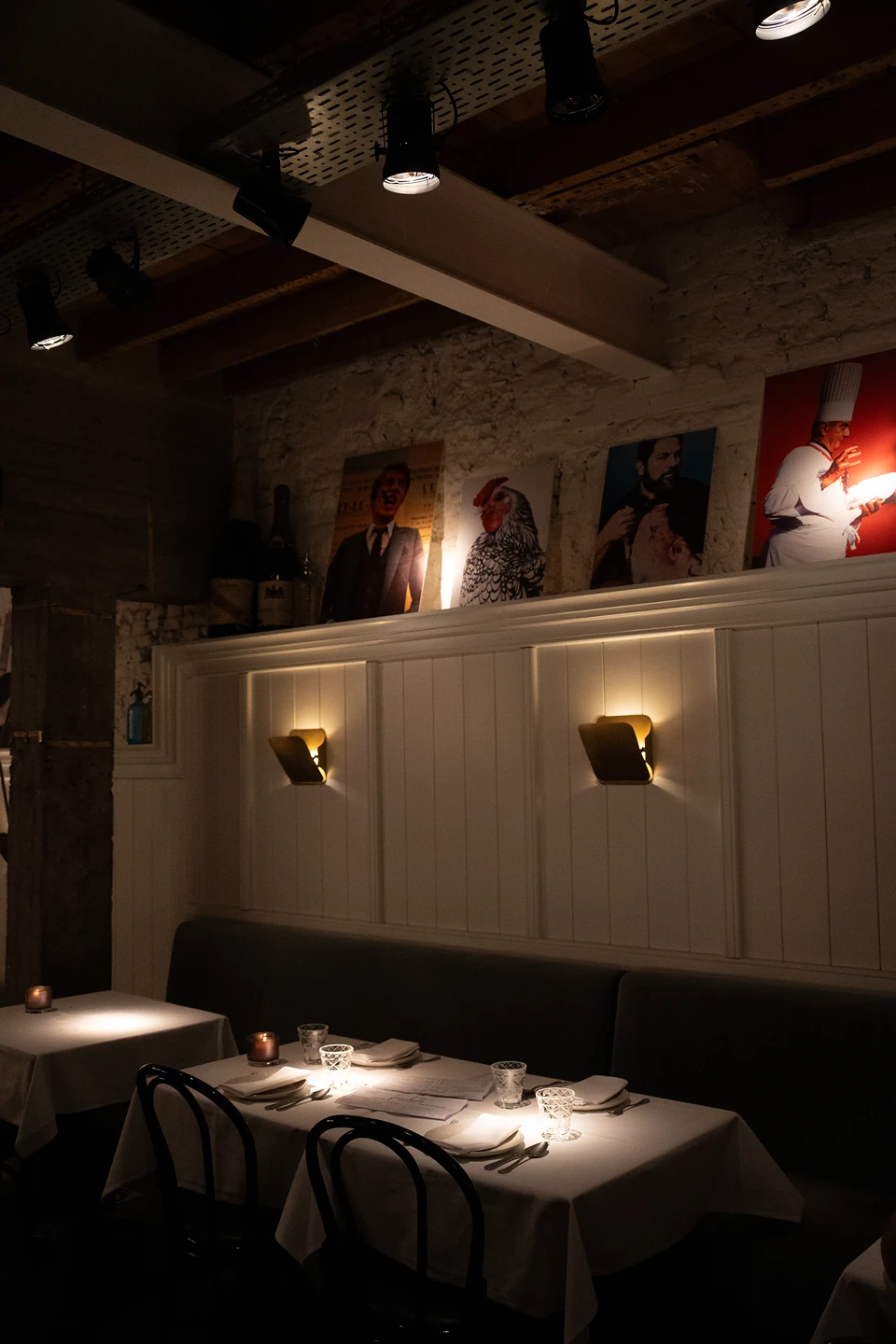 Empty tables laid for dinner in a dark corner, spotlights on the posters above