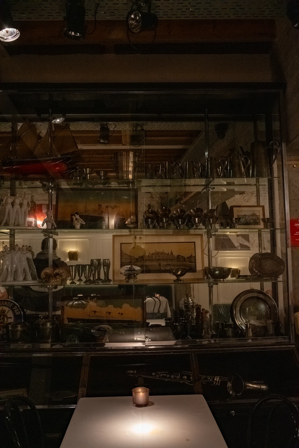 A glass cabinet of pewter, figurines and old framed prints behind a candlelit table